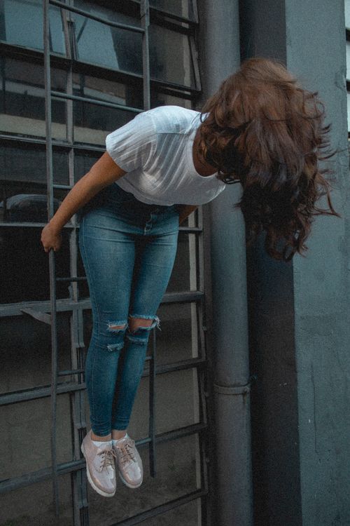 Free Woman posing creatively on a ladder against urban backdrop. Stock Photo