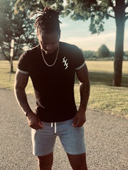 Fashionable tattooed man in casual attire stands outdoors during the day, showing style and confidence.