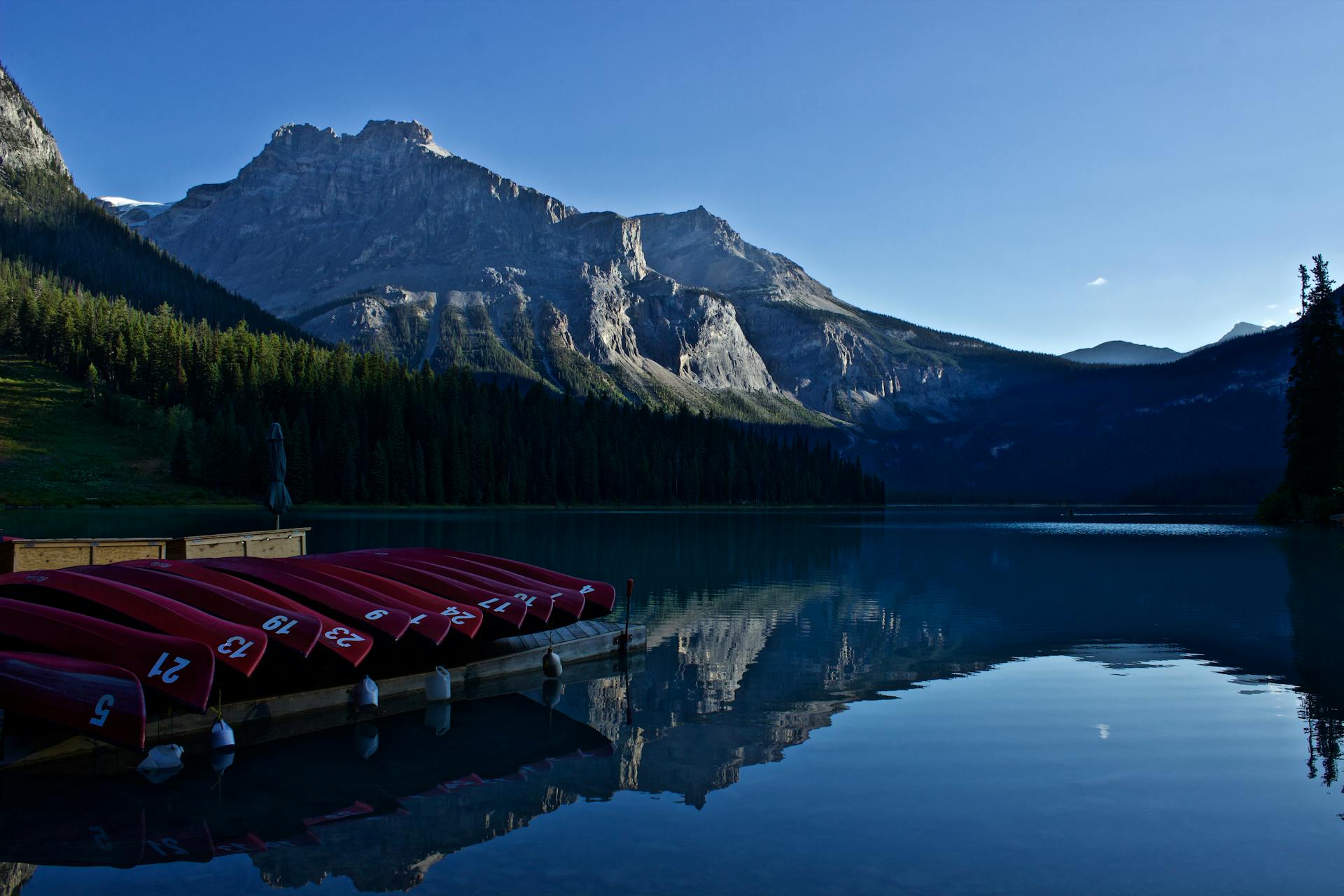 A serene mountain landscape featuring a calm lake and red canoes at dawn under a clear sky.