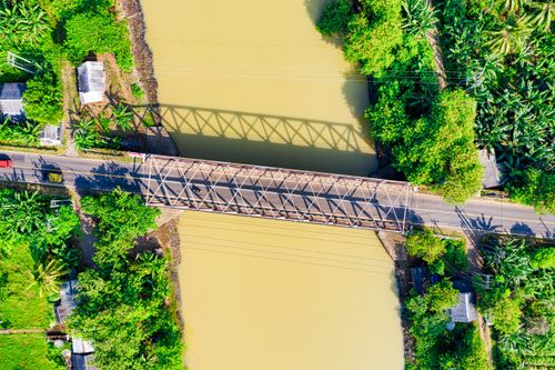 Free Aerial shot showing a bridge crossing a river amidst lush tropical greenery and some rural infrastructure. Stock Photo