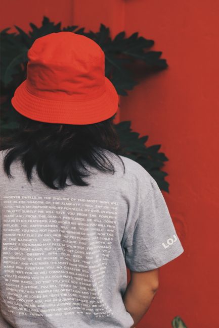Back view of a person wearing a red bucket hat and graphic tee against a red wall.