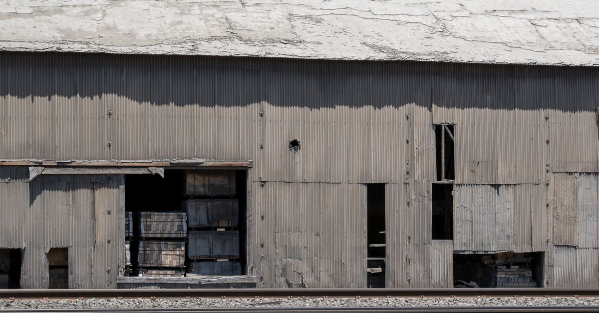 Image of an old, abandoned warehouse with broken walls next to railway tracks in Monolith, CA.