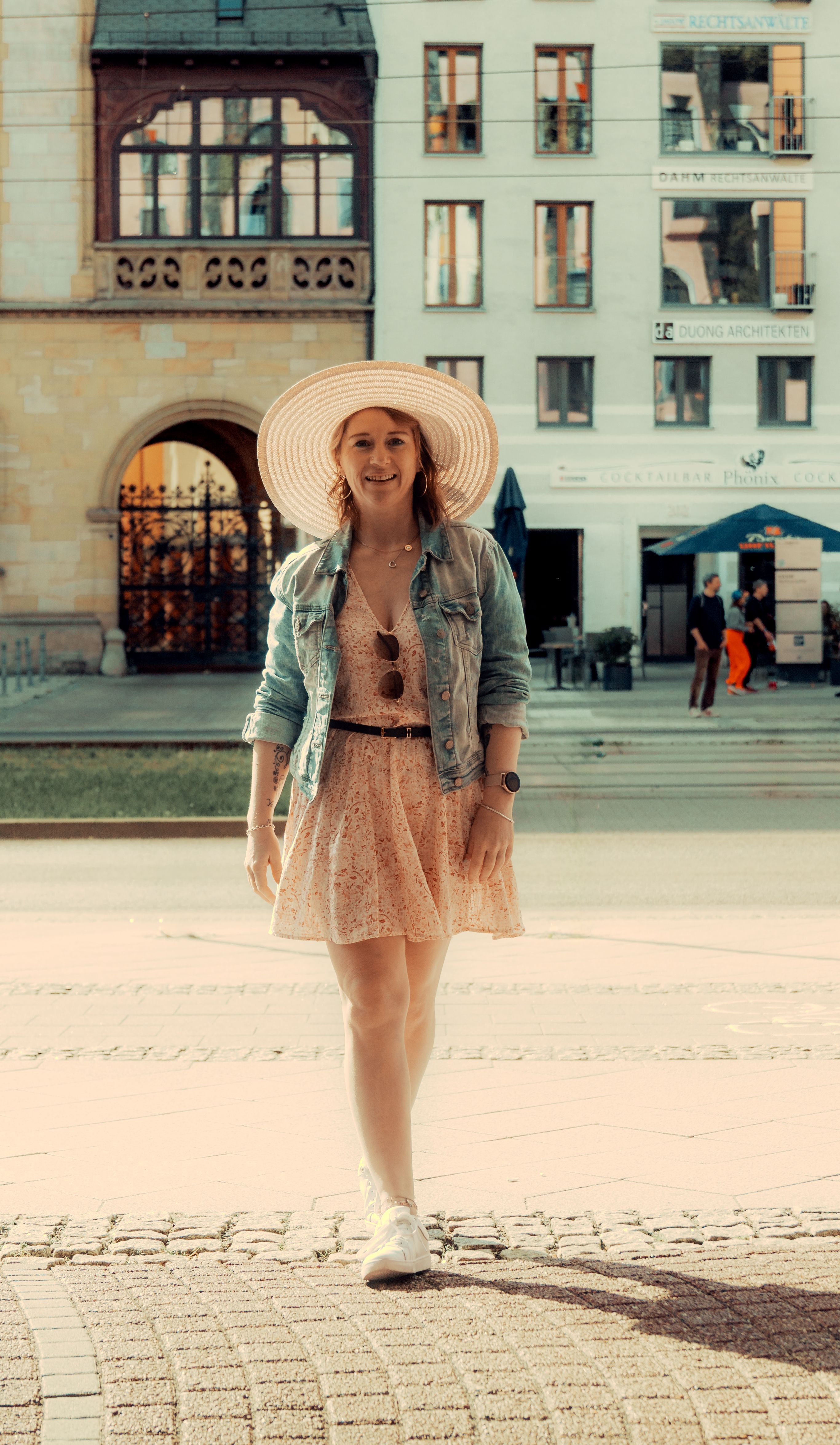 Confident woman in a dress and hat strolling through urban Magdeburg on a sunny day.
