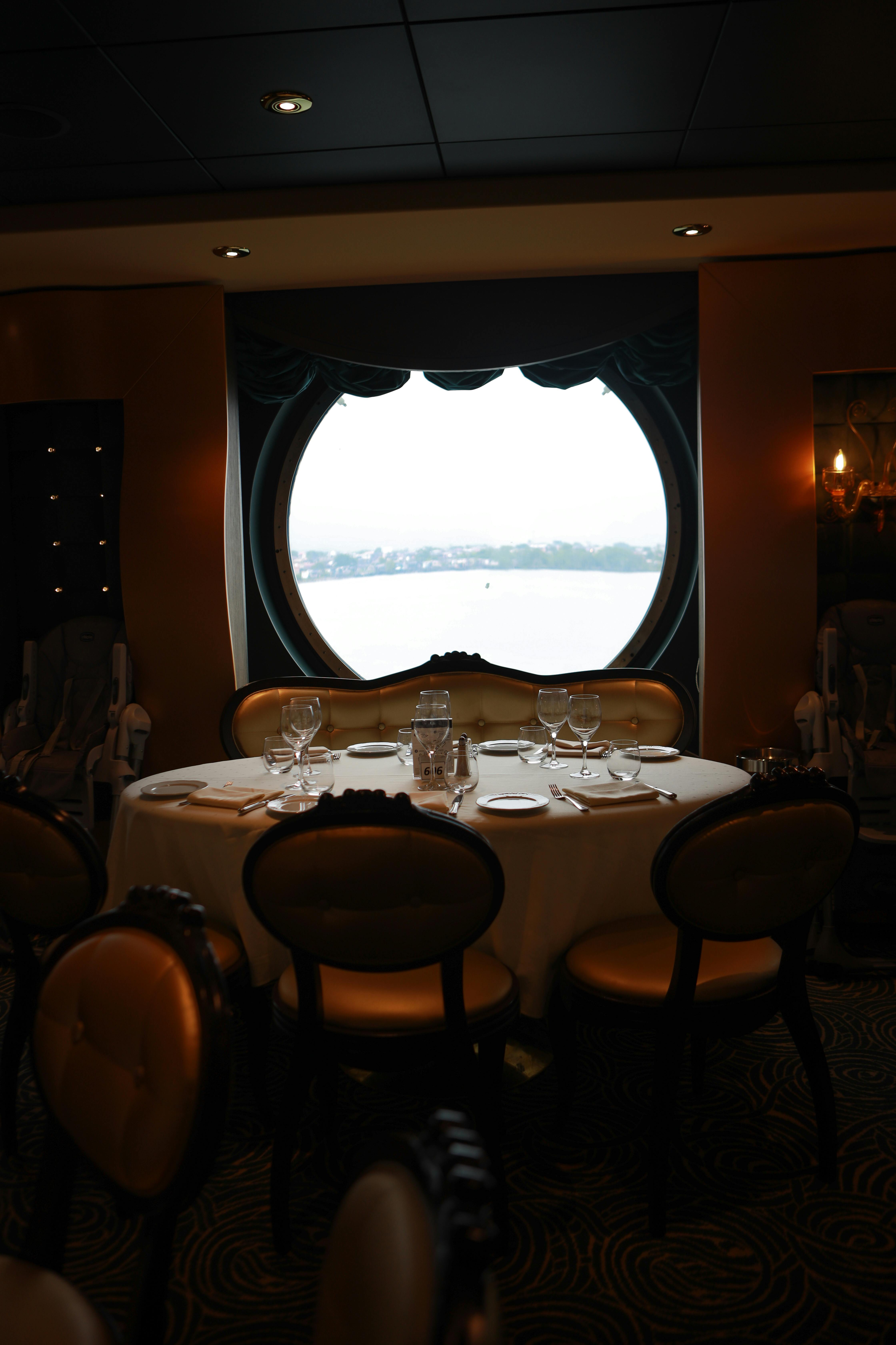 Elegant dining area on a cruise ship with a stunning ocean view through a round window.