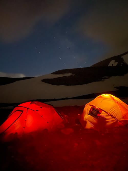Two tents lit up at night on a mountain