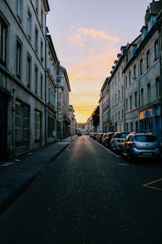 黄昏时分，宁静的城市街道上，明亮的天空下停着汽车，旁边是经典建筑