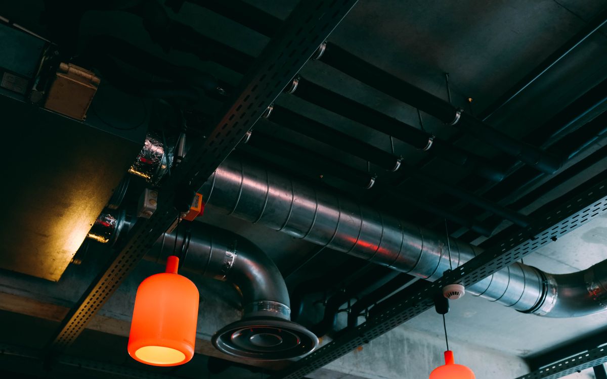 Low-angle view of a modern industrial ceiling featuring ducts and red lamps.