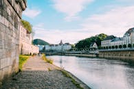 人们沿着风景优美的河畔小路行走，那里有历史建筑，头顶是明亮的蓝天