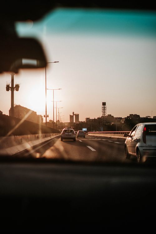Free View from car windshield as vehicles travel on an urban highway at sunset. Stock Photo