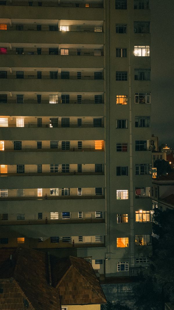 Vista externa de um prédio de apartamentos em São Paulo com janelas iluminadas à noite.