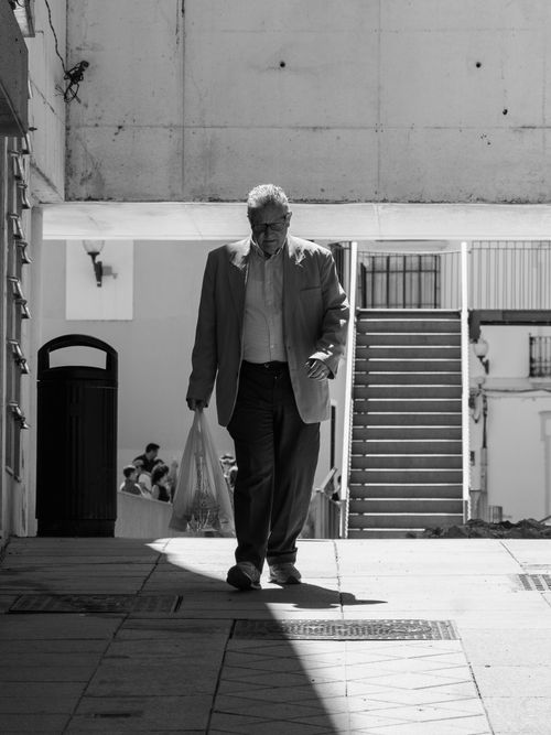 Free Senior man carrying groceries in a city setting, captured in black and white. Stock Photo
