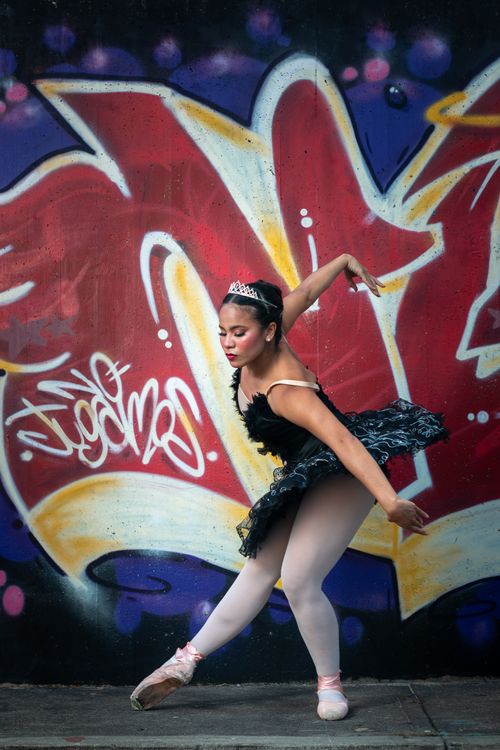 Free Young ballerina in black tutu posing gracefully in front of vibrant graffiti mural outdoors. Stock Photo