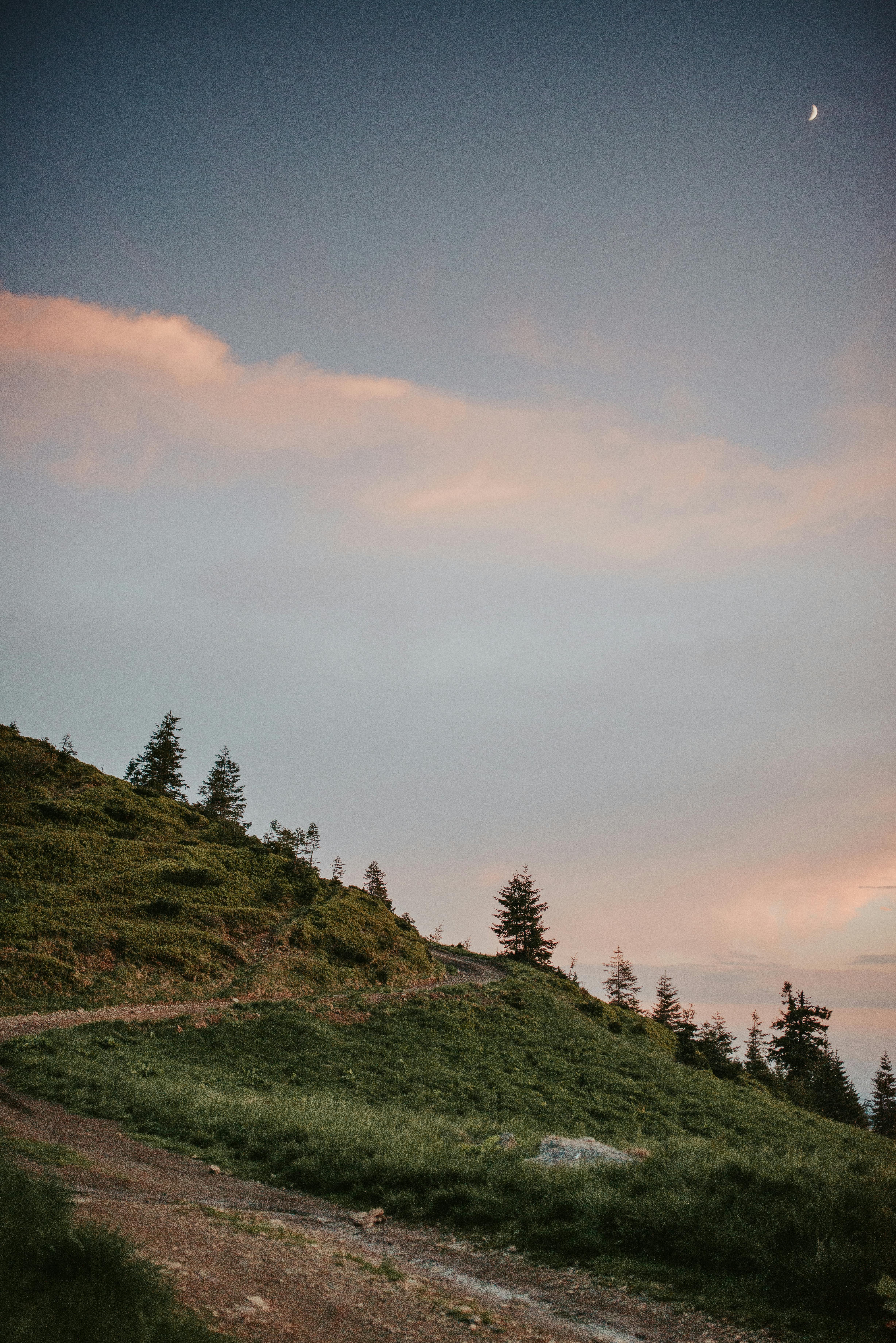 暮色中，新月低垂，一条宁静的土路蜿蜒穿过连绵起伏的青山
