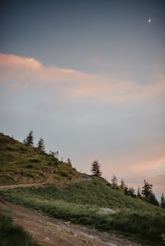 暮色中，新月低垂，一条宁静的土路蜿蜒穿过连绵起伏的青山