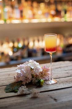 Glass of fresh cold cocktail and flowers placed on wooden table in restaurant