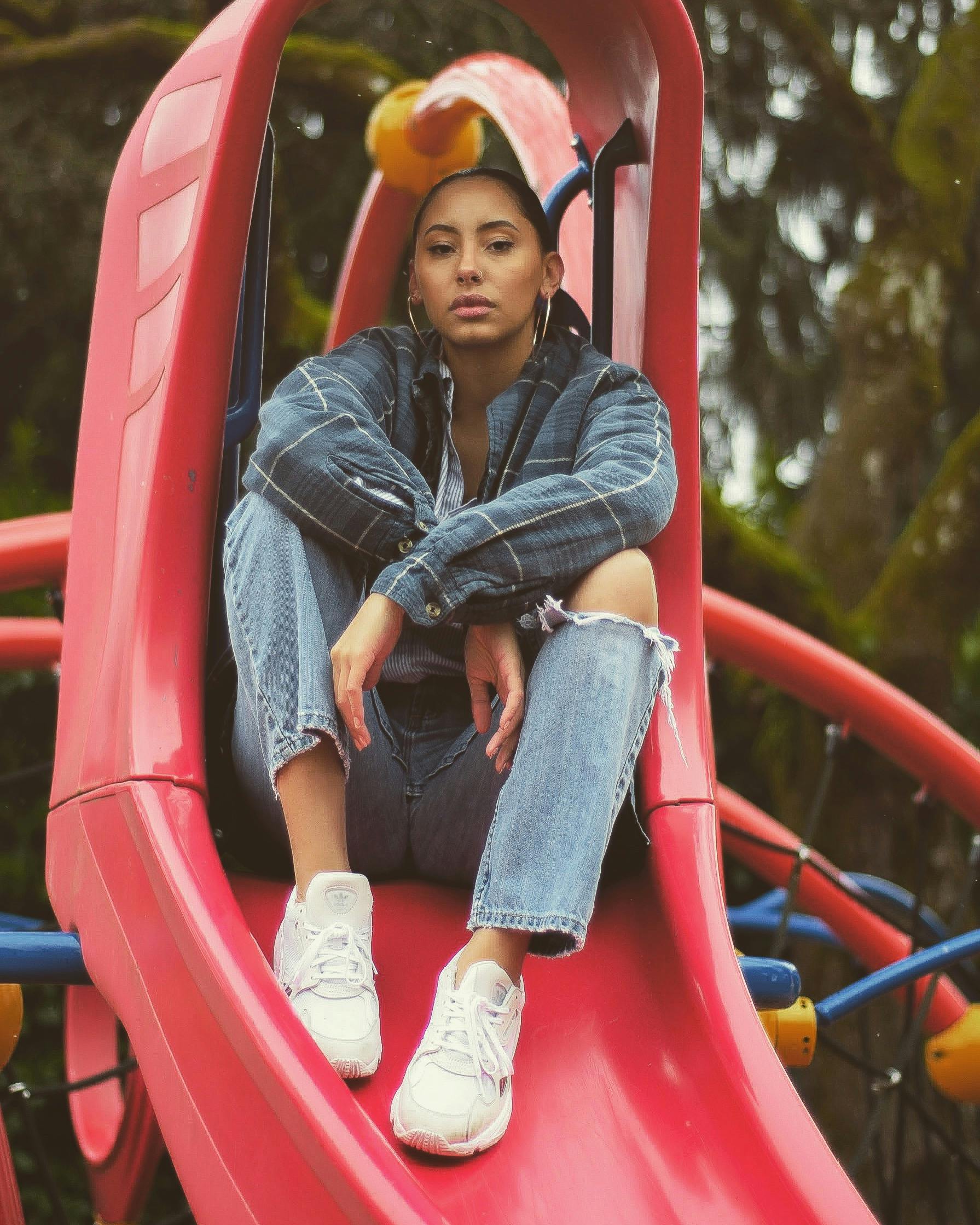 一位时尚女士穿着休闲牛仔装，在户外操场的滑梯上摆姿势