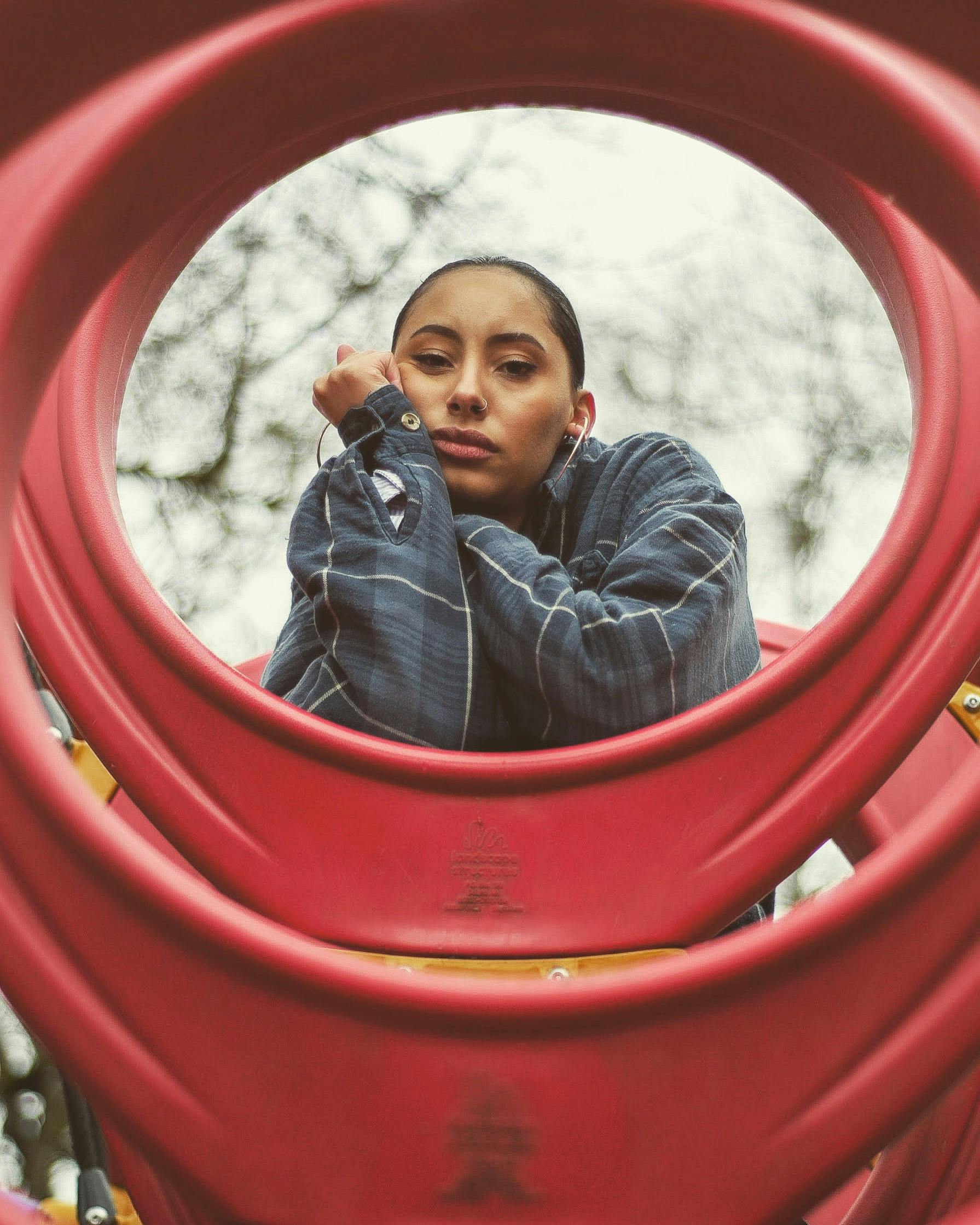 在户外彩色游乐场管道的映衬下，一位年轻女子摆出深思熟虑的姿势