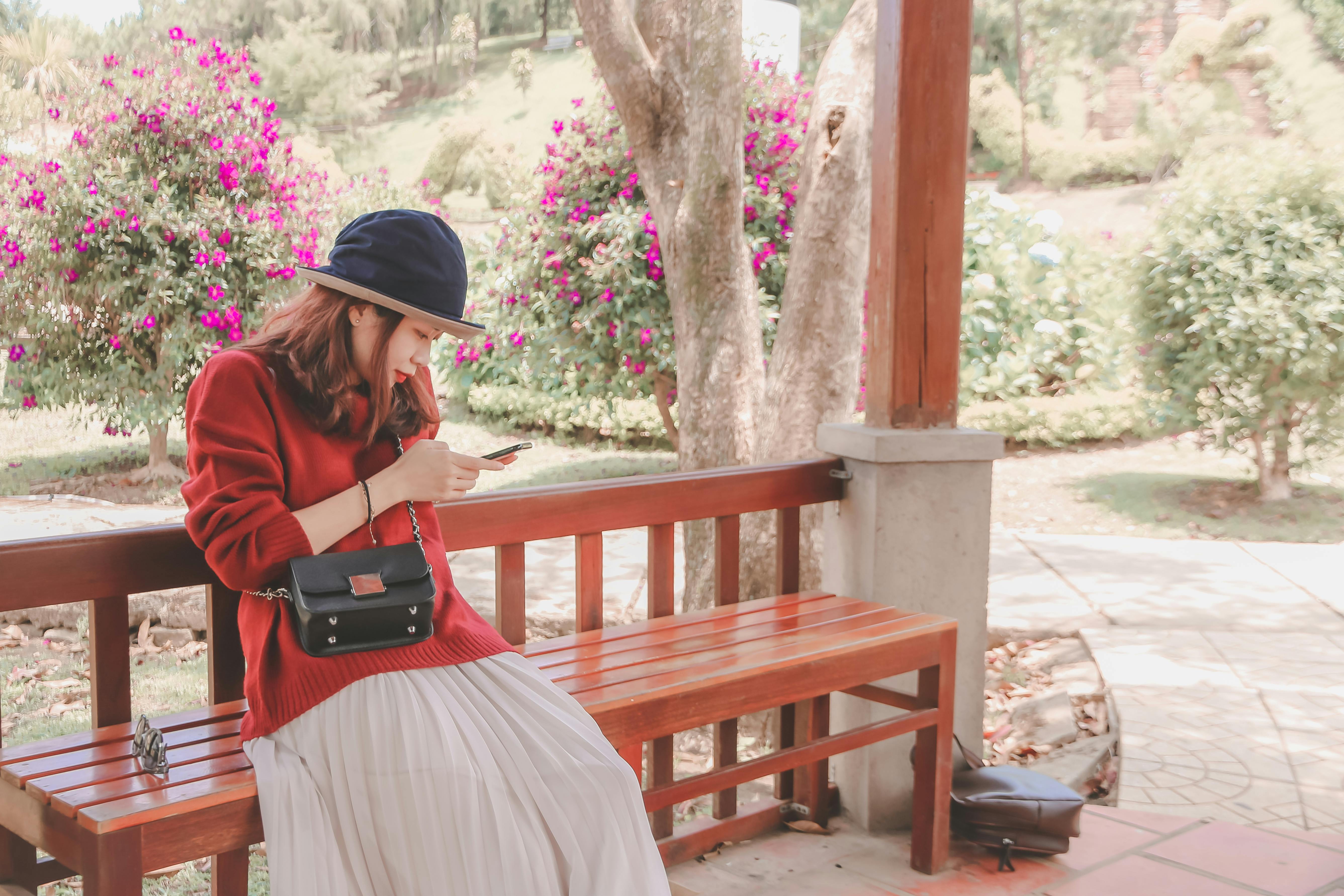 一位亚洲女子坐在花园的木凳上，一边放松身心，一边用智能手机享受独处时光