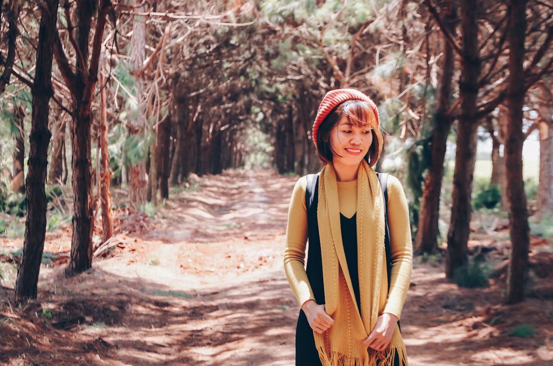 Photo of Smiling Woman Walking Alone Along Trail Between Trees