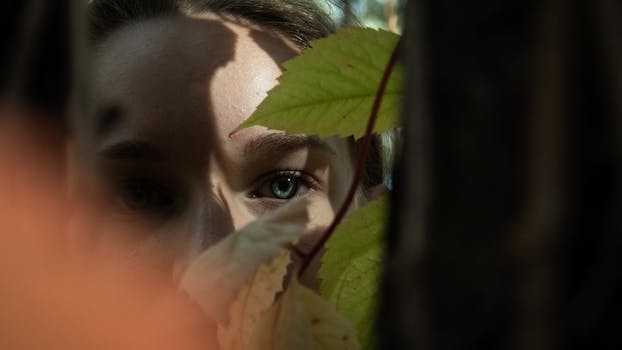 透过树叶窥视的女人眼睛特写，营造出一种神秘的氛围