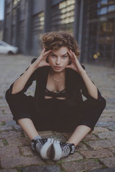 Young woman with short hair posing outdoors on a cobblestone street, wearing a stylish black outfit.