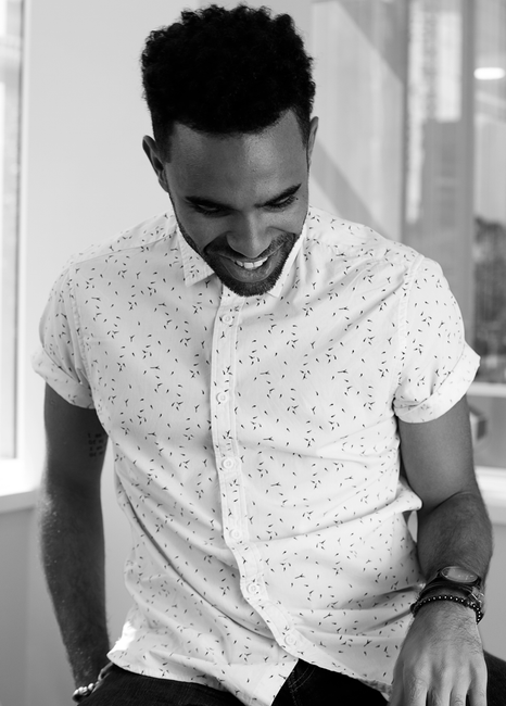 Black and white portrait of a smiling man in a stylish patterned shirt, captured indoors.