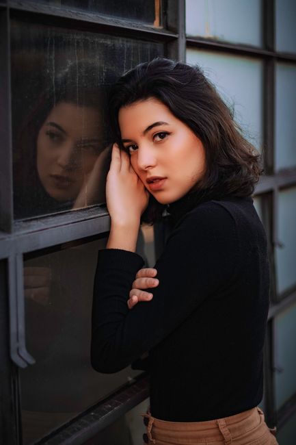Portrait of a fashionable woman leaning against a glass window, exuding elegance and style.