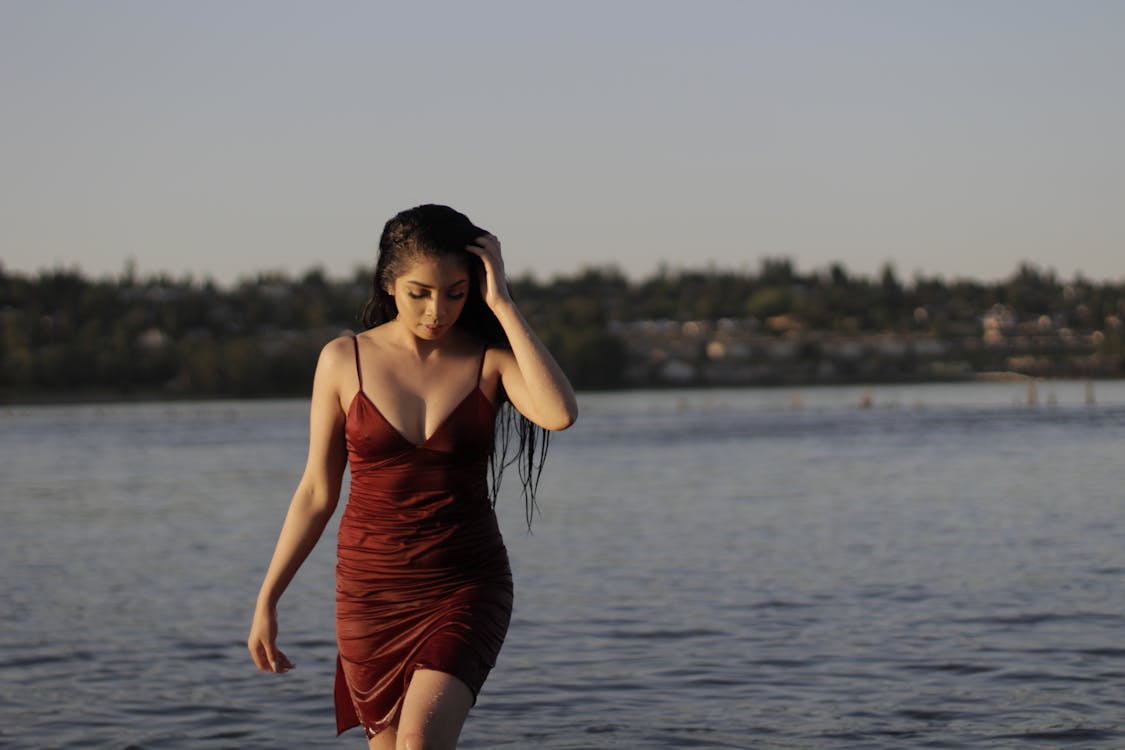 Free Photo of Woman in Red Spaghetti-strap Dress Walking out from Body of Water Looking Down Stock Photo
