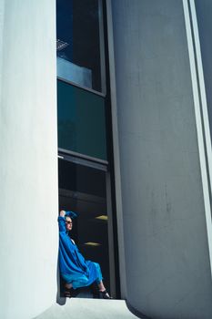 白天，一位身穿蓝色服装的时尚女子在现代建筑前摆姿势