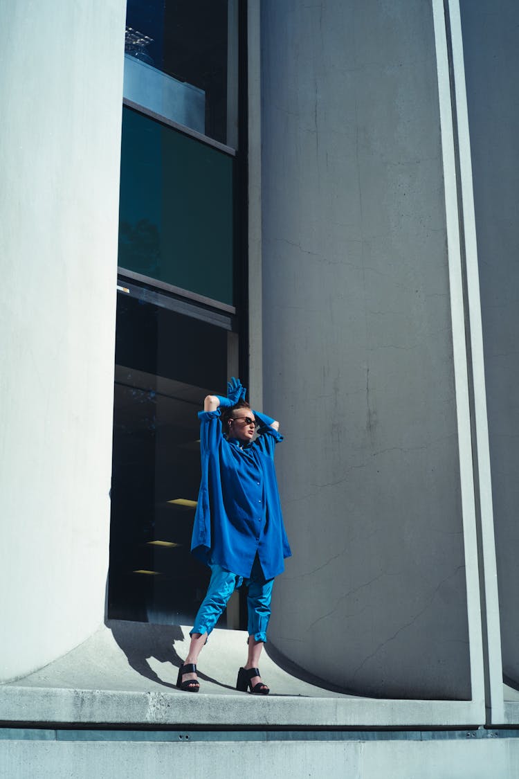 Person In Blue Top And Blue Pedal Short Standing By The Building Glass Window