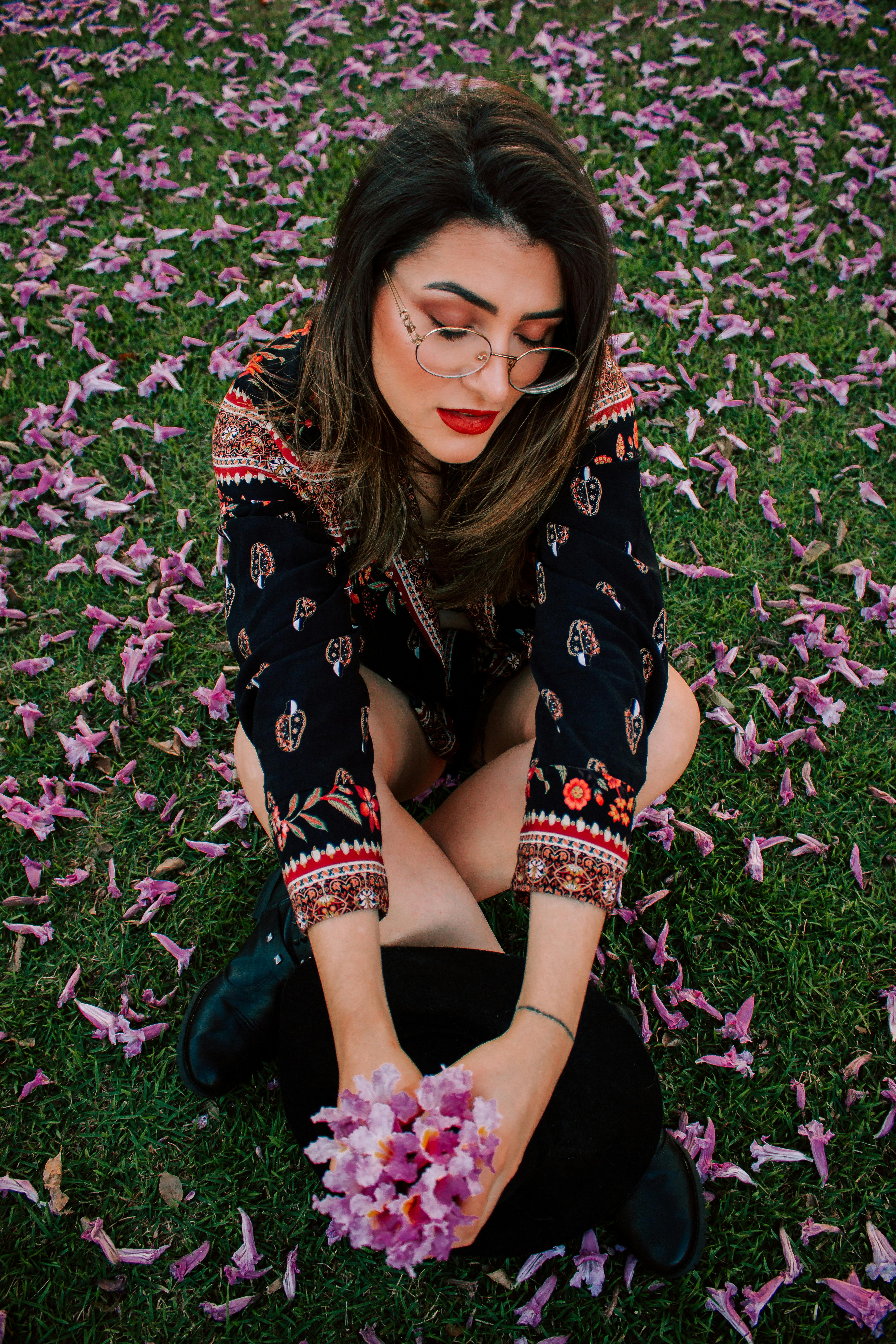 一位穿着印花连衣裙的美丽女子，在户外盛开的花瓣中手持一朵紫色的花