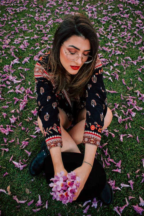 Bezpłatne Kobieta Ubrana W Czarną Bluzkę Siedzi Na Trawie Trzymając Kwiaty Zdjęcie z galerii