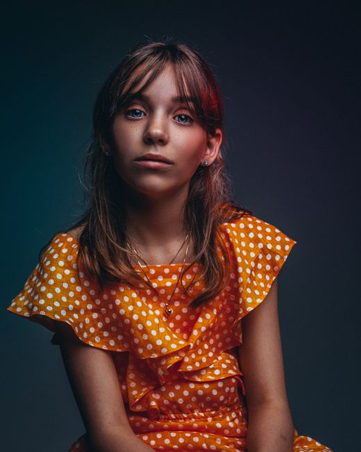 Artistic portrait of a girl wearing a polka dot dress with a dramatic lighting background.