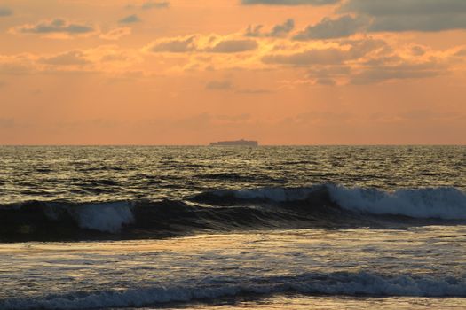 Beautiful ocean sunset with vibrant clouds and waves reflecting the golden hues of the evening sky.
