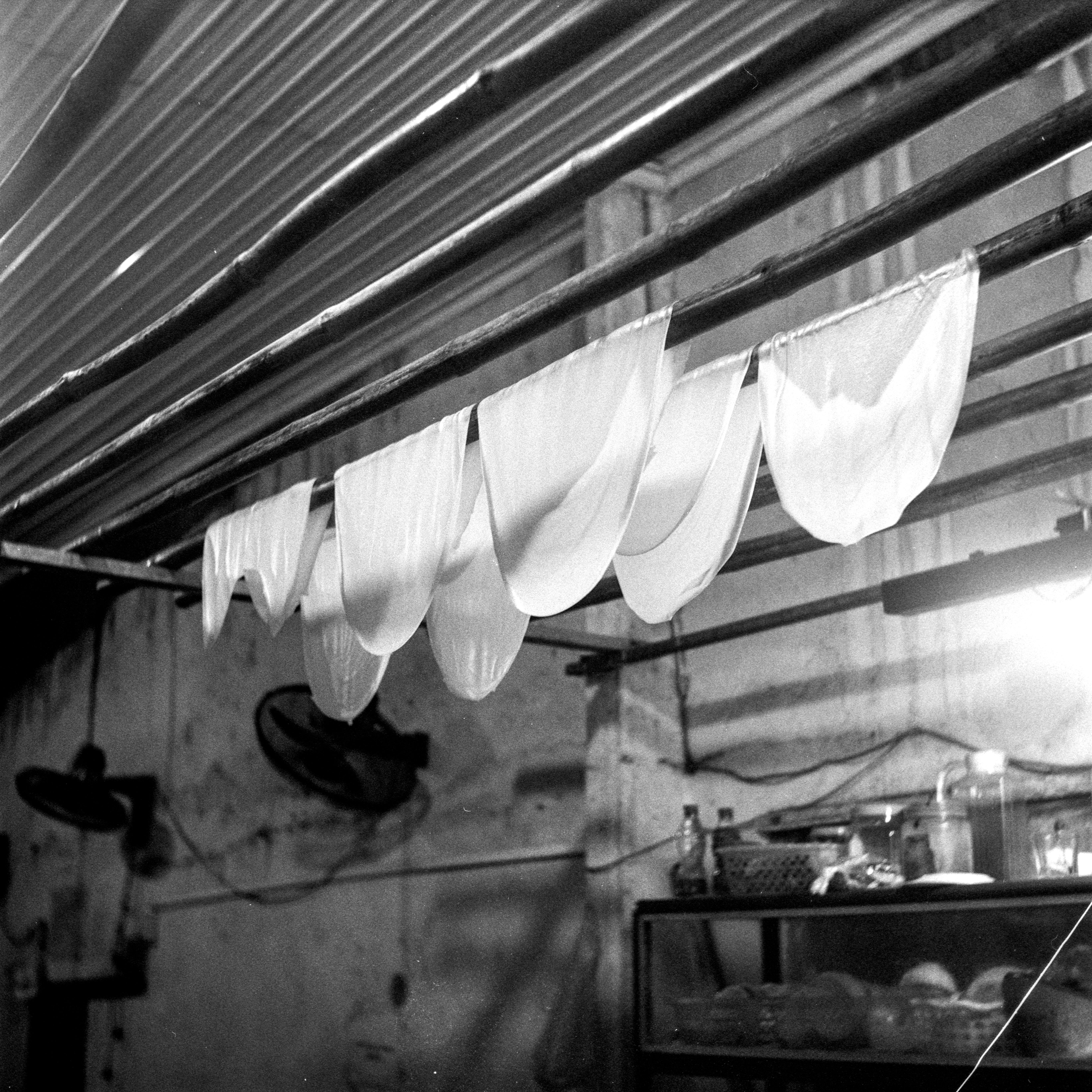 Black and white photo of sheets drying indoors on wooden poles.
