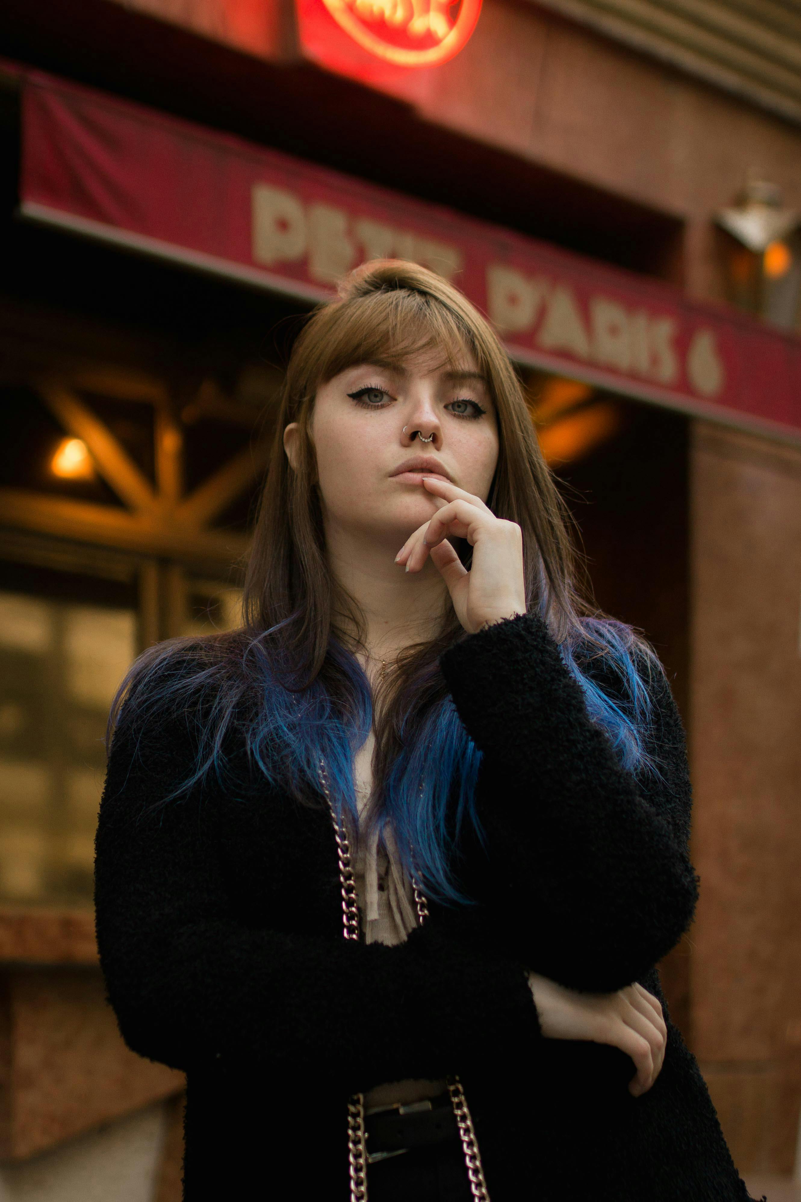 一位深色头发、点缀着蓝色亮点的时尚女性，在城市户外自信地摆出姿势