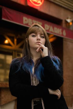 一位深色头发、点缀着蓝色亮点的时尚女性，在城市户外自信地摆出姿势