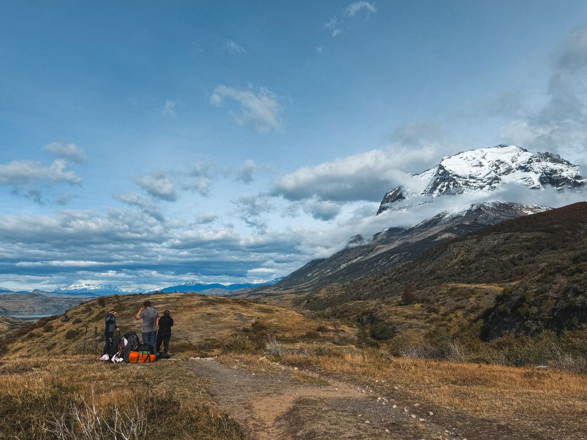 A group of hikers trek through scenic snowcapped mountains and dry grasslands, embracing outdoor adventure.