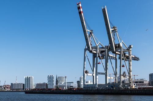 Free Wide-angle view of cargo cranes at Hamburg harbor with urban skyline. Stock Photo