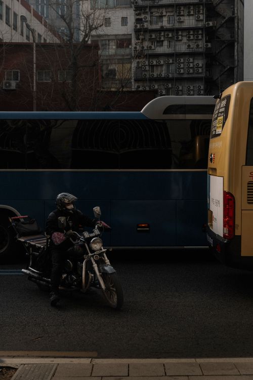 Free A motorcyclist waits in city traffic beside buses on a busy street. Stock Photo