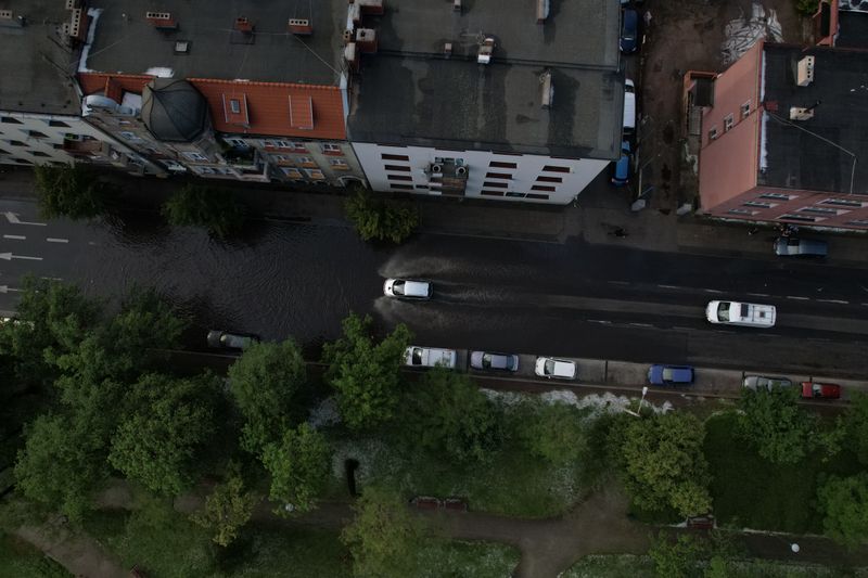 Cars navigate through a flooded street in an urban area, captured from above.