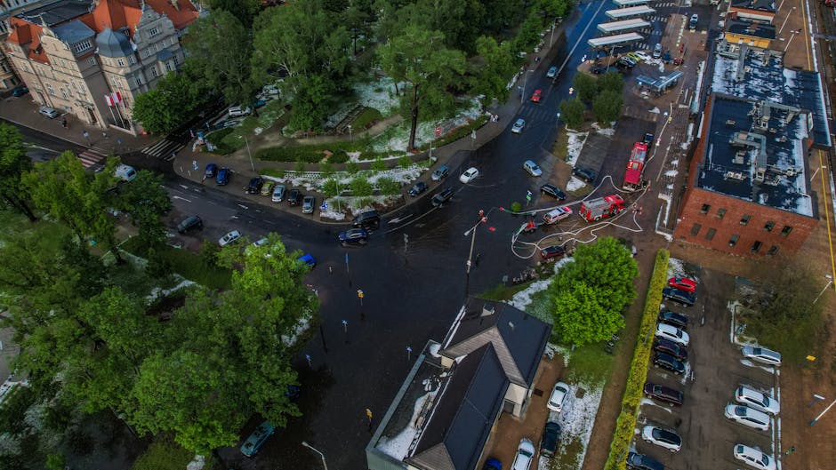 Aerial view of a flooded city intersection surrounded by greenery and buildings after a hailstorm with fire trucks responding.