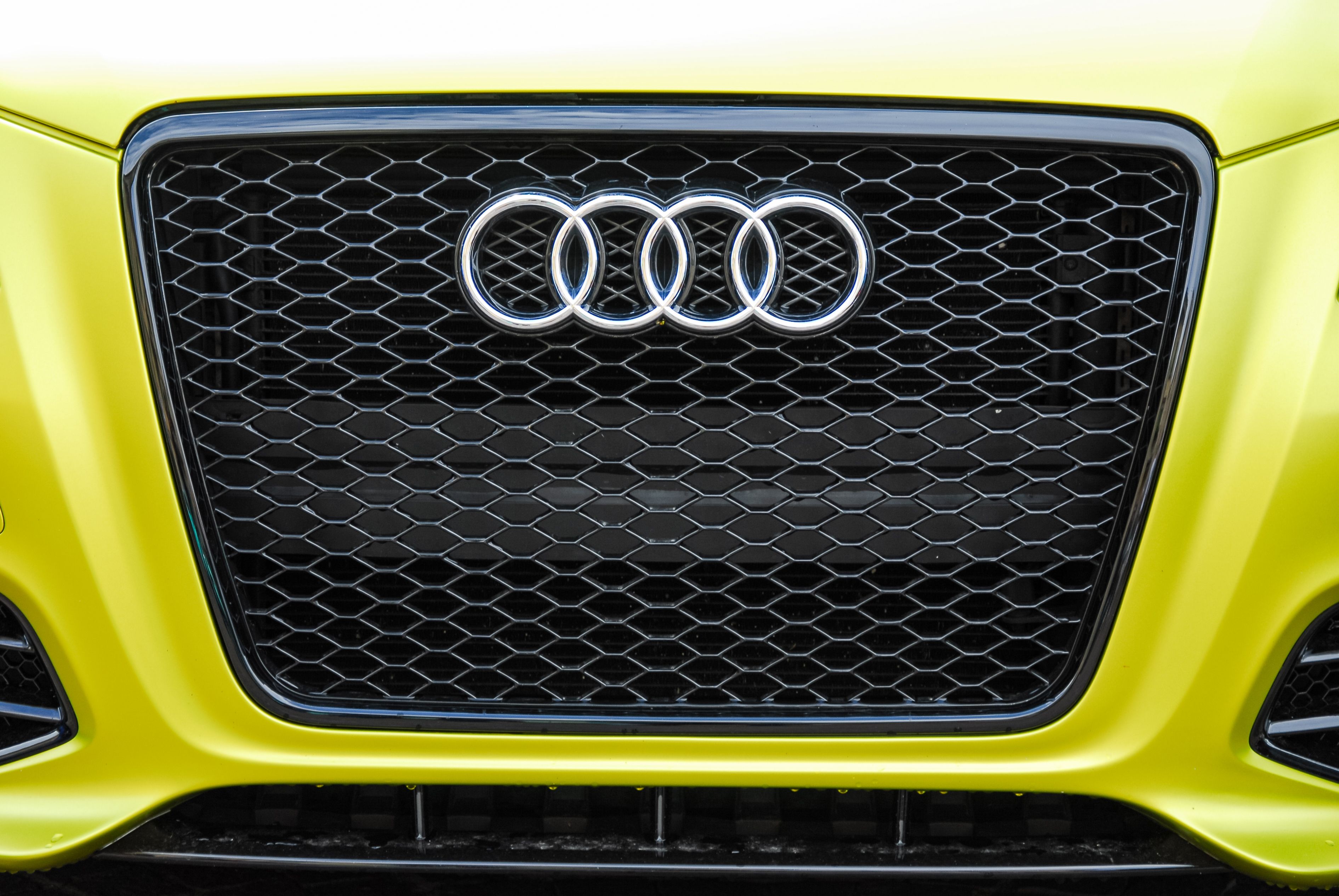 Close-up of a sleek Audi car grille in vivid yellow, showcasing design and luxury.