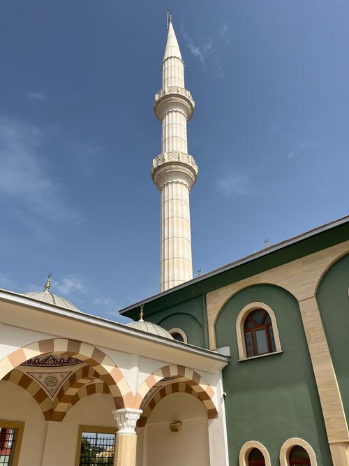 Free A tall mosque minaret surrounded by traditional Islamic architecture under a clear blue sky. Stock Photo