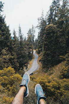 从独特的角度拍摄，鸟瞰蜿蜒道路穿过郁郁葱葱的森林，前景是鞋子
