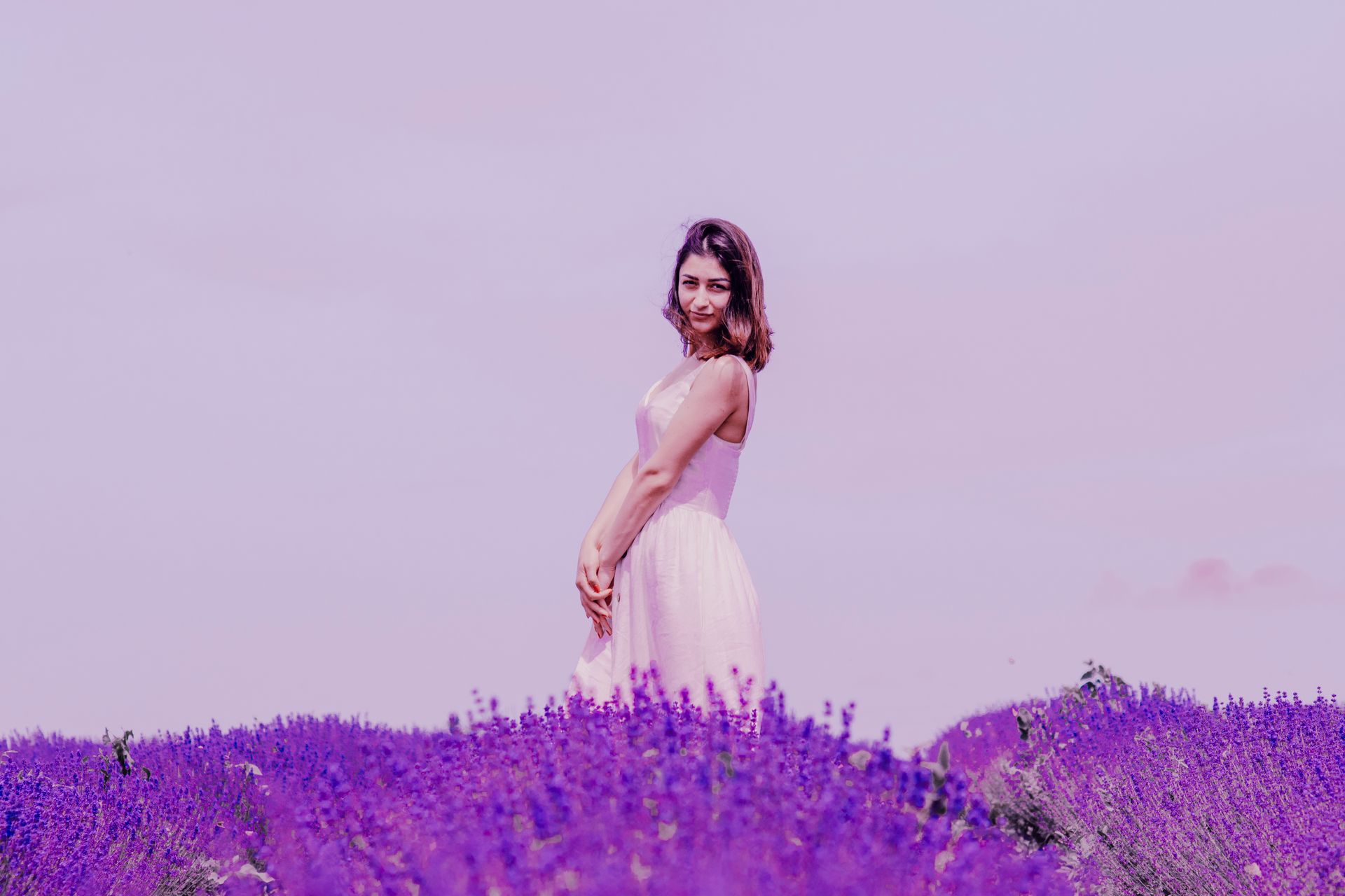 Woman in a flowing dress posing amidst a vibrant lavender field on a sunny day.