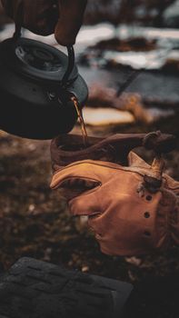 Close-up of a person pouring tea from a kettle into a cup during a camping trip outdoors.