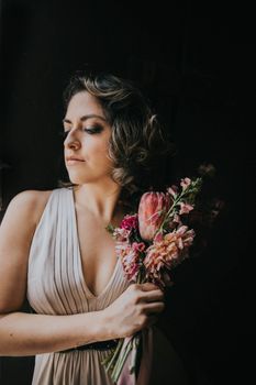 Sophisticated woman holding bouquet in elegant pose against dark backdrop.