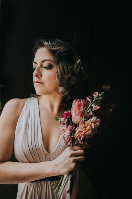 Sophisticated woman holding bouquet in elegant pose against dark backdrop.