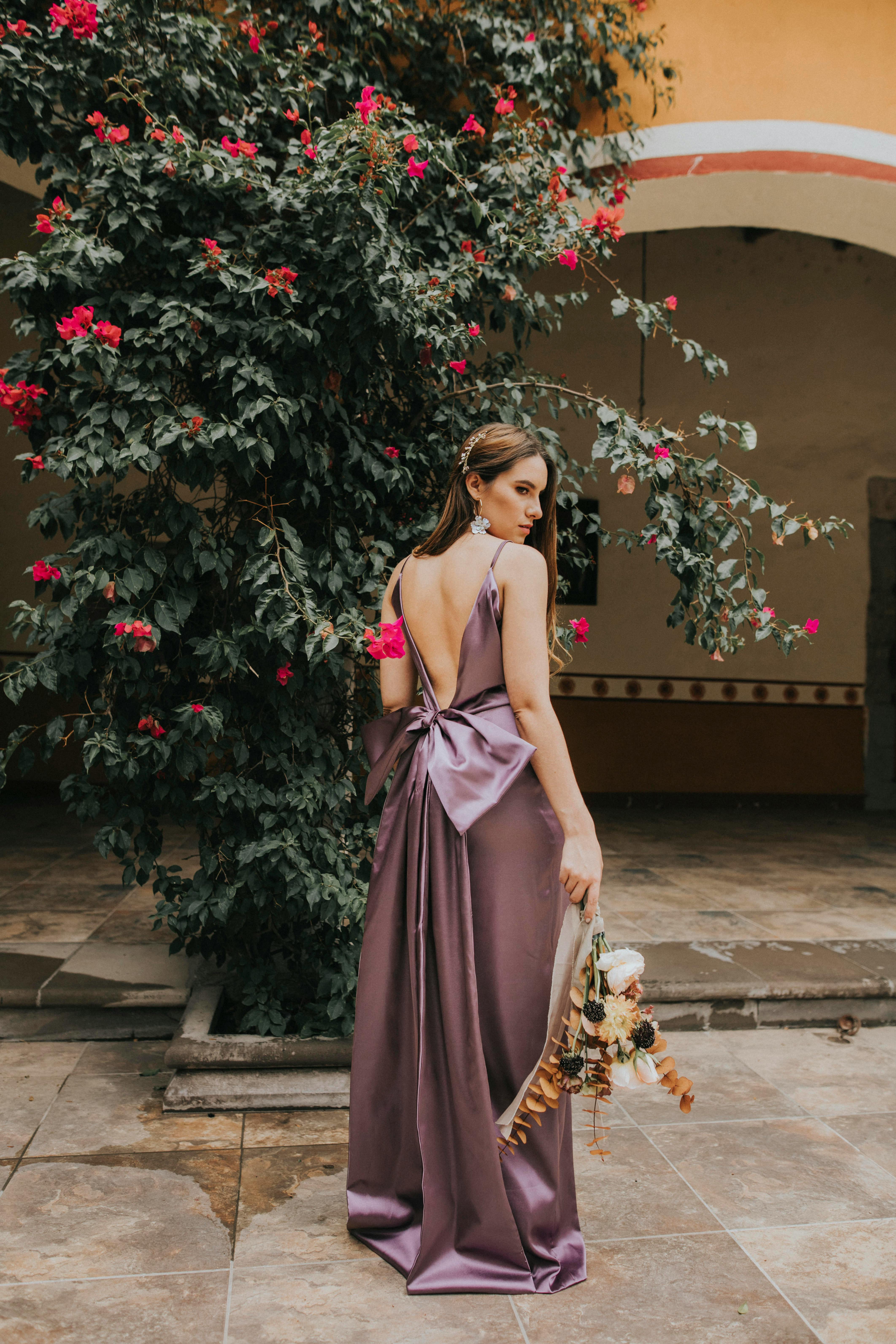 一位身着紫色礼服的时尚女士，在花卉背景前手持花束摆出姿势，非常适合时尚优雅的主题